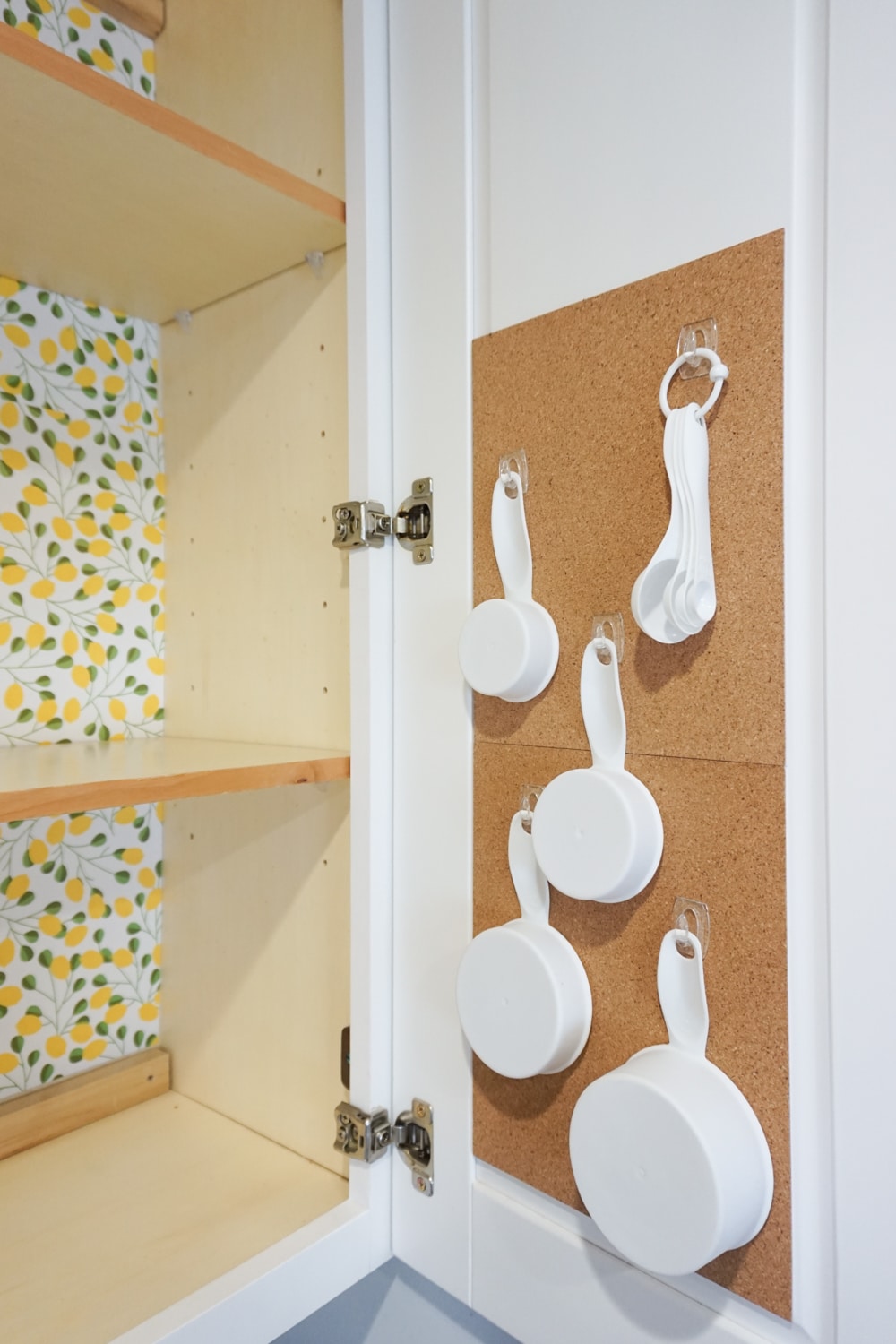Organizing baking supplies is easy with cork tiles, command hooks, vinyl labels, and a beautiful craft paper to line the cabinet.