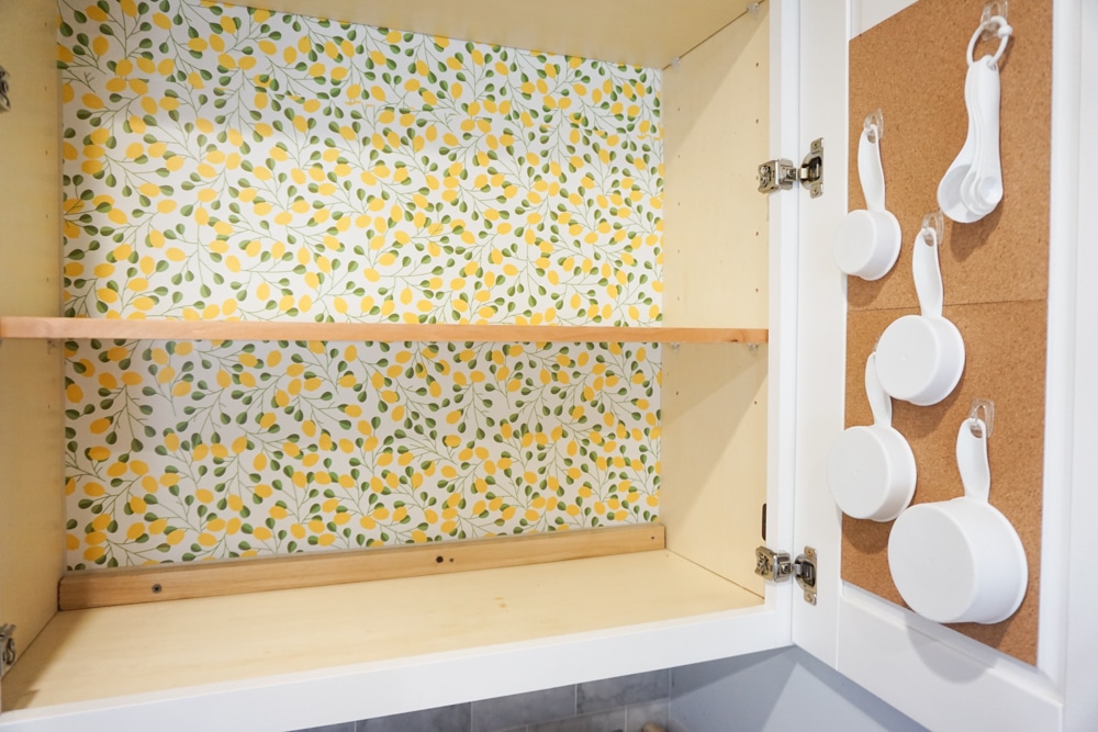 Organizing baking supplies is easy with cork tiles, command hooks, vinyl labels, and a beautiful craft paper to line the cabinet.